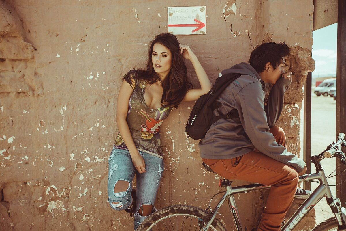 Bruna Ramos Del Nero encostada na parede ao lado de um garoto de bicicleta. Estão usando roupas da moda teen.